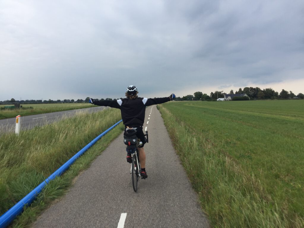 Ein Mann auf einem Fahrrad auf einem Radweg der seine Arme im 90° Winkel von sich Streckt.